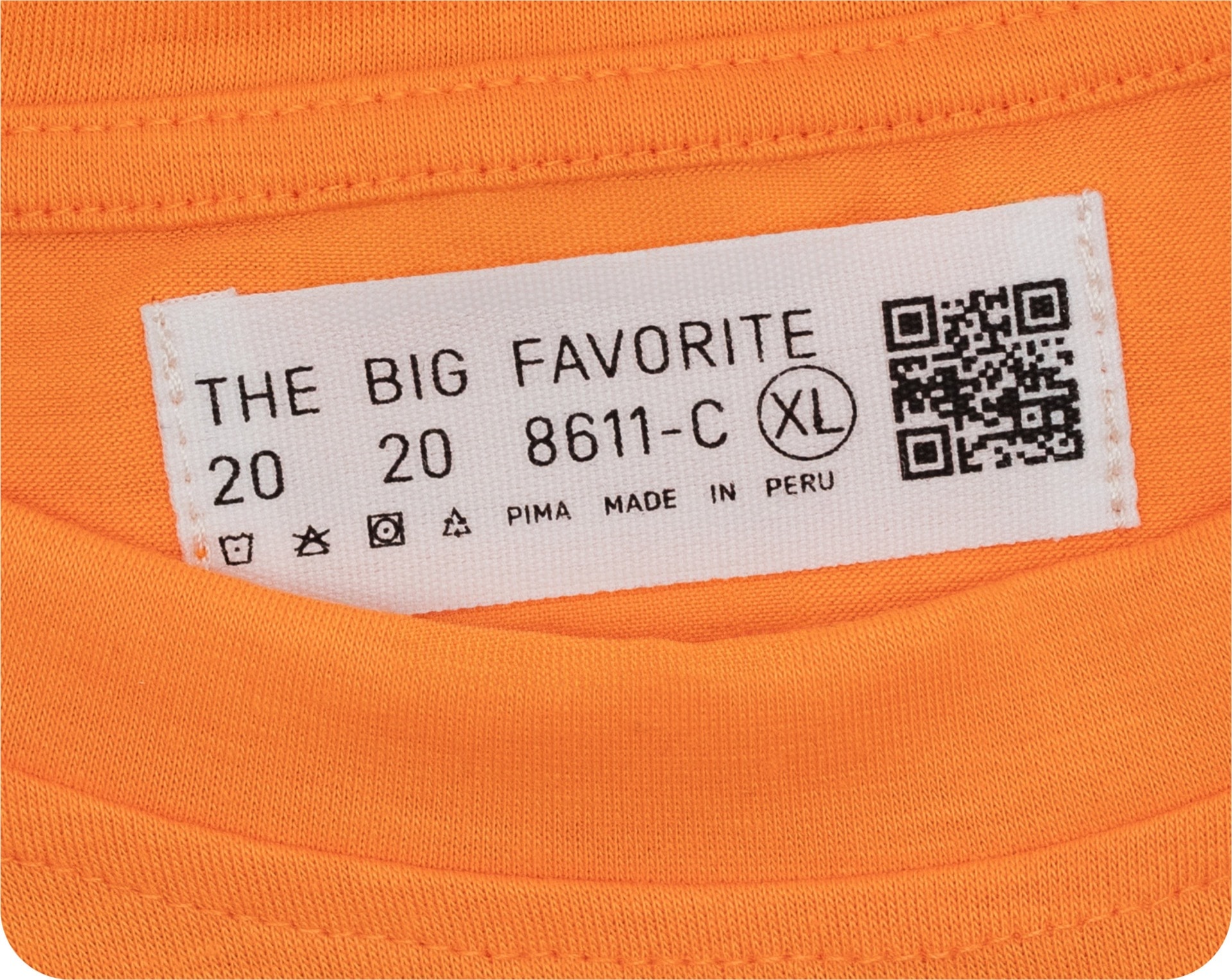 A printed cotton care label with text, a QR code, and washing symbols on an orange t-shirt.
