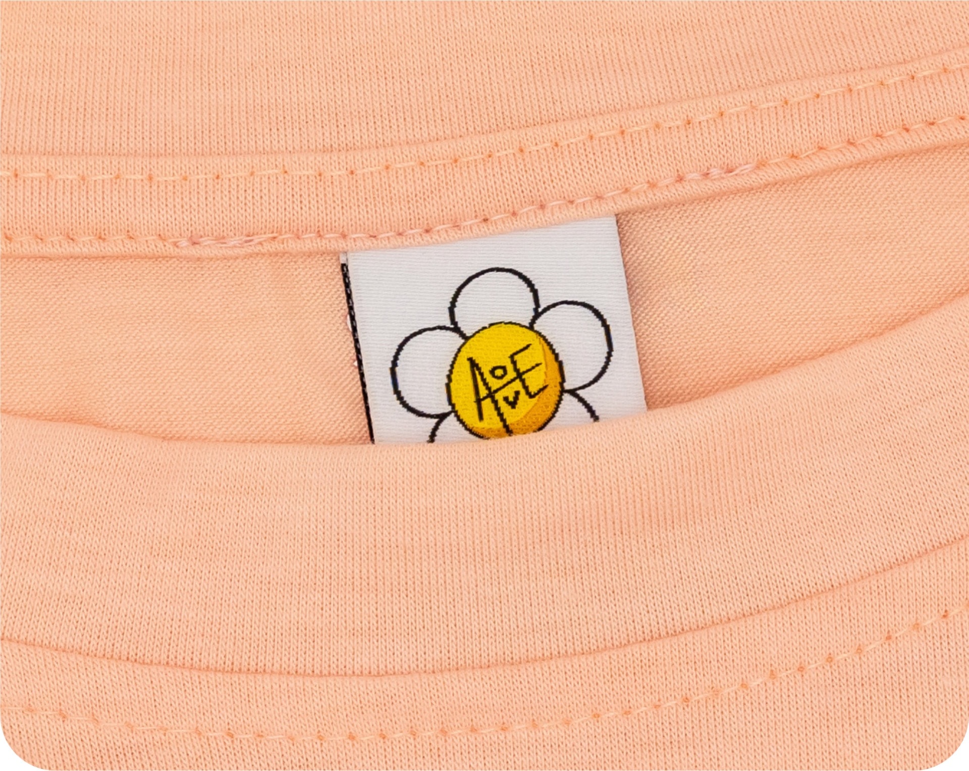 A custom woven label with a yellow and white flower design sewn into a peach-colored garment.
